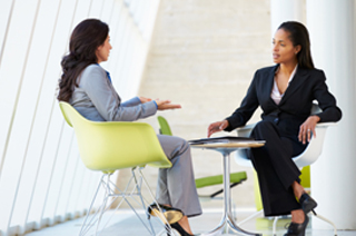 Image of two business women seated at a table having a discussion